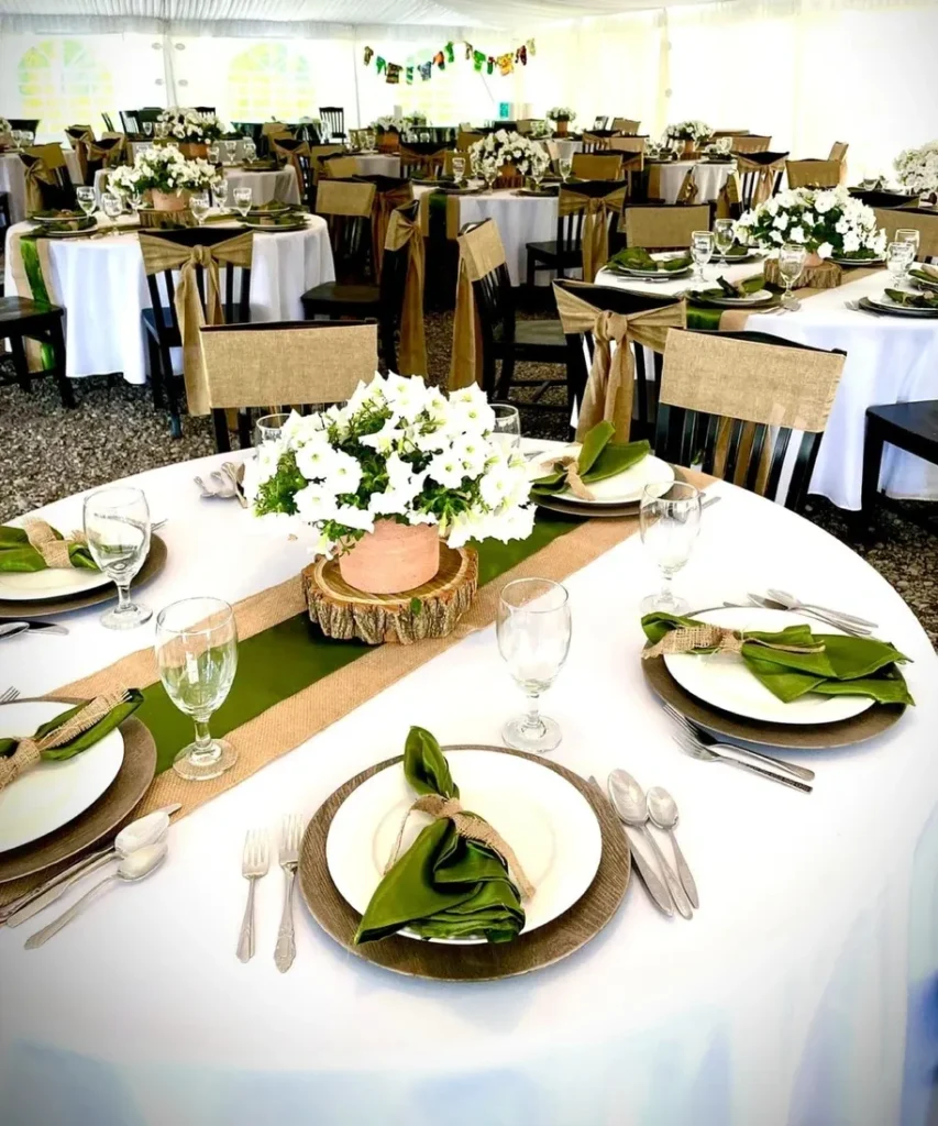 Elegant wedding reception setup at Riverbend Events in Weedsport, NY, featuring white tablecloths, green napkins, rustic burlap accents, floral centerpieces, and neatly arranged glassware and silverware under a tent for special occasions.