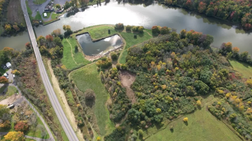 Aerial view of Riverbend Events venue in Weedsport, NY, showcasing lush green trees, a winding river, open grassy areas, and a nearby road, highlighting the natural beauty and outdoor spaces ideal for weddings and special occasions.