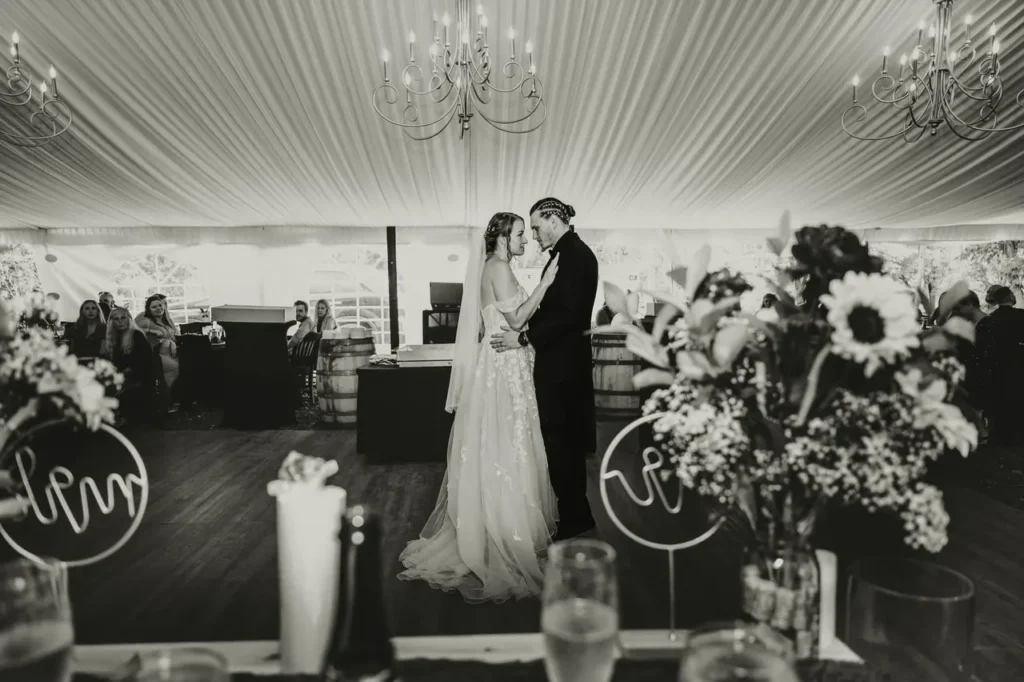 Bride and groom sharing a first dance in an elegant, draped indoor wedding venue at Riverbend Events in Weedsport, NY, surrounded by seated guests, floral arrangements, and soft natural light, highlighting a personalized and intimate wedding experience.