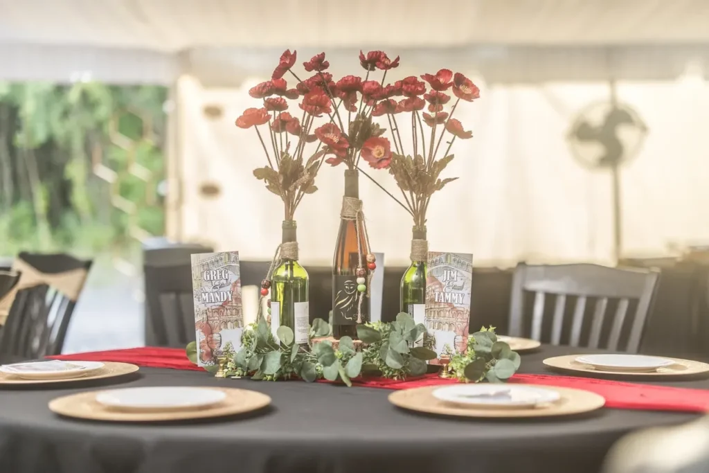 Wedding reception table featuring floral centerpieces in wine bottles, elegant plates on wooden chargers, and personalized name cards, showcasing the venue’s focus on personalized, elegant wedding experiences with natural and indoor-outdoor settings.